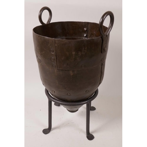 62 - A riveted metal urn with two ring handles on a wrought iron stand, 13