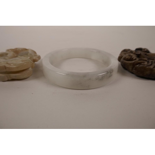 12 - A Chinese grey jade bangle and two carved hardstone pendants decorated with mythical figures, bangle... 