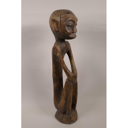 22 - An African carved wood tribal figure seated with hands on knees, 19