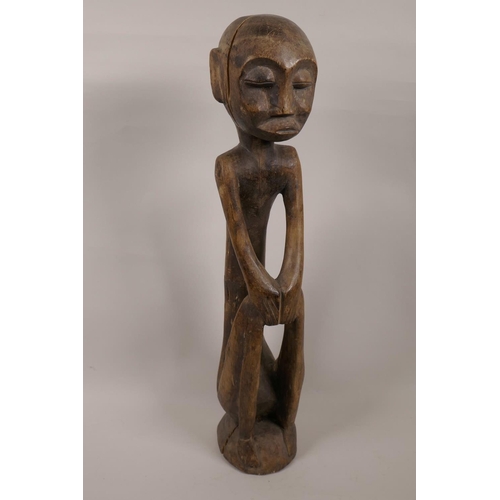 22 - An African carved wood tribal figure seated with hands on knees, 19