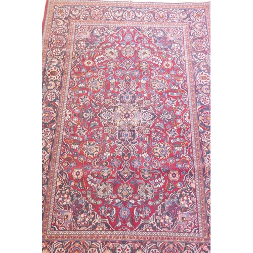 1184 - A vintage Kashan hand knotted wool carpet with central medallion design and blue borders on a red fi... 