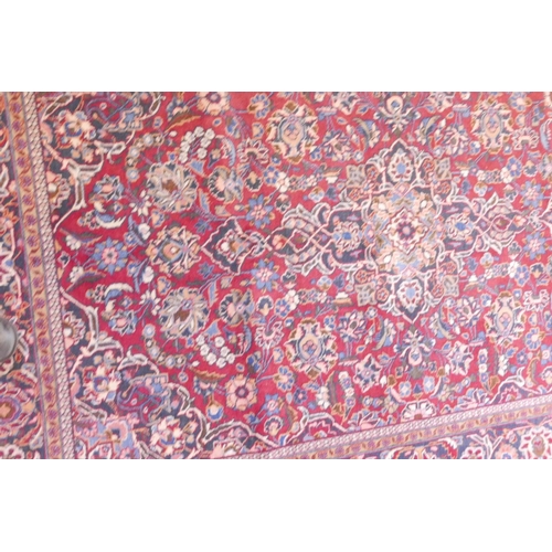 1184 - A vintage Kashan hand knotted wool carpet with central medallion design and blue borders on a red fi... 