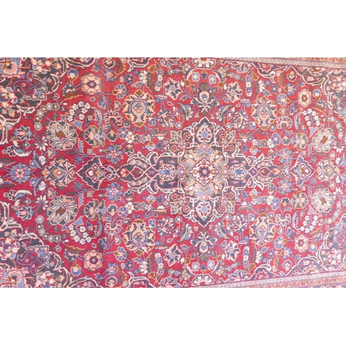 1184 - A vintage Kashan hand knotted wool carpet with central medallion design and blue borders on a red fi... 