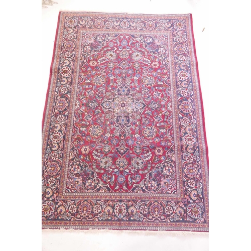 1184 - A vintage Kashan hand knotted wool carpet with central medallion design and blue borders on a red fi... 