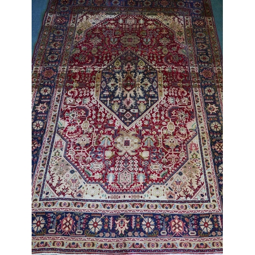 1198 - A red ground Persian Tabriz carpet with a traditional design and blue ground border, 118