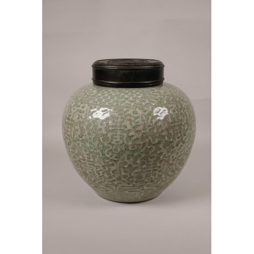 23 - A Chinese green glazed crackleware jar with a turned wood cover, the body with raised auspicious sym... 