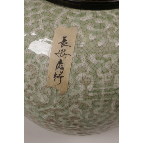 23 - A Chinese green glazed crackleware jar with a turned wood cover, the body with raised auspicious sym... 