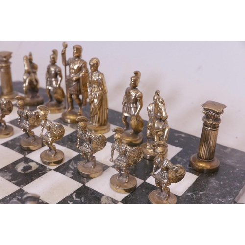 31 - A gilt and white metal chess set, the figures cast as classical Romans, on a marble board, 16