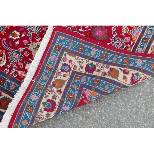 1131 - A red ground full pile Persian village rug with all over floral decoration to the central field, 50