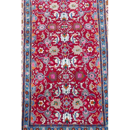 1131 - A red ground full pile Persian village rug with all over floral decoration to the central field, 50