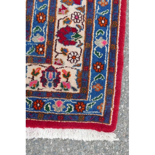 1131 - A red ground full pile Persian village rug with all over floral decoration to the central field, 50