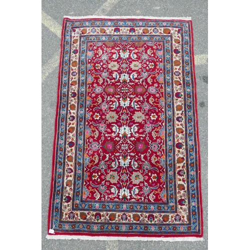 1131 - A red ground full pile Persian village rug with all over floral decoration to the central field, 50