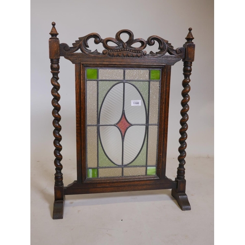 1108 - A 1930s oak firescreen with carved decoration and barleytwist supports, fitted with leaded light gla... 