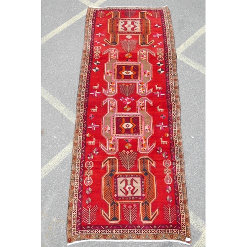 1126 - A Persian wool runner with a geometric medallion design on a rich red field, 52