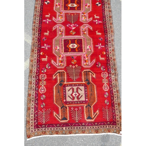 1126 - A Persian wool runner with a geometric medallion design on a rich red field, 52