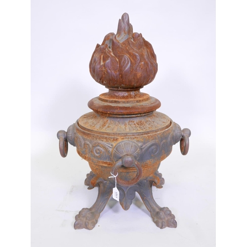 1101 - A C19th cast iron urn with four ring handles, raised on paw feet, the cover cast as a flame, 29