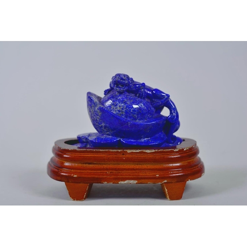 64 - A Chinese carved lapis ornament in the form of a kylin atop a money token, on a wood stand, 6