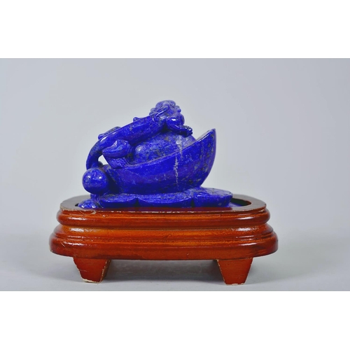 64 - A Chinese carved lapis ornament in the form of a kylin atop a money token, on a wood stand, 6