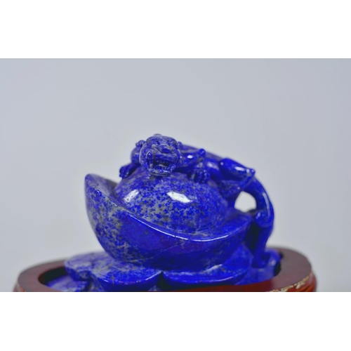 64 - A Chinese carved lapis ornament in the form of a kylin atop a money token, on a wood stand, 6