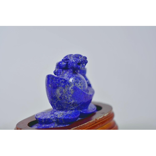 64 - A Chinese carved lapis ornament in the form of a kylin atop a money token, on a wood stand, 6