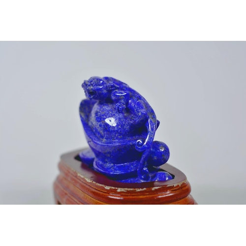 64 - A Chinese carved lapis ornament in the form of a kylin atop a money token, on a wood stand, 6