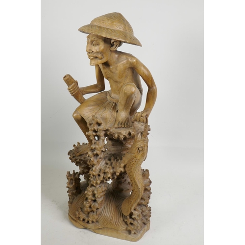 47 - An oriental carved wood figure of a fisherman with large fish, seated on a coral reef, 21