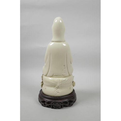 40 - A Chinese blanc de chine porcelain Quan Yin seated on a lotus flower, on a carved and pierced hardwo... 