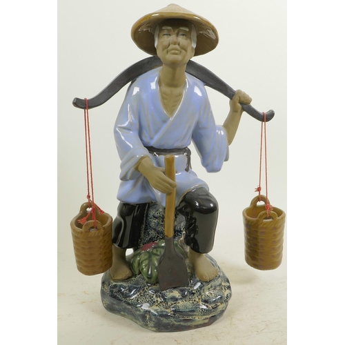 366 - A Chinese, Shiwan style, mud men figure of a workman seated on a rock with his shovel and baskets, 1... 