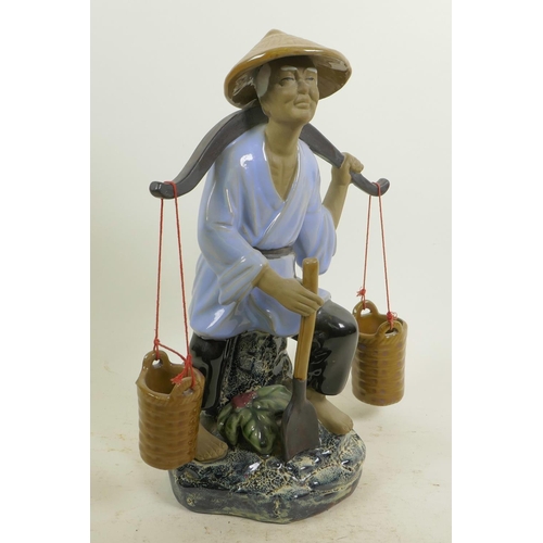 366 - A Chinese, Shiwan style, mud men figure of a workman seated on a rock with his shovel and baskets, 1... 