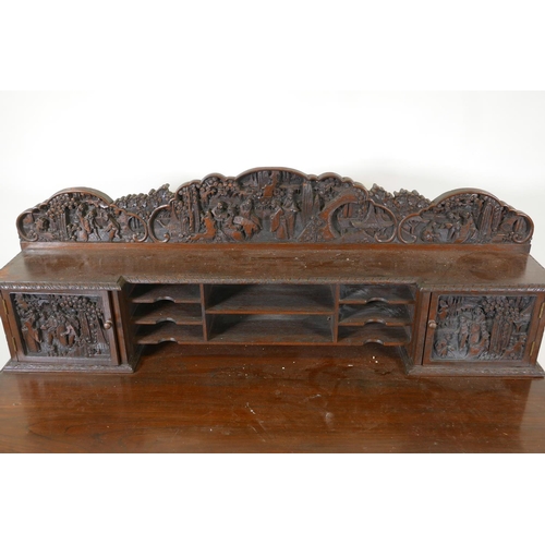 1003 - A Chinese carved hardwood desk, the raised upper section with two small cupboards and pigeon holes, ... 