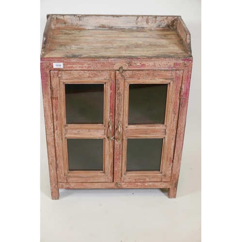 1039 - An Indian hardwood cabinet with two glazed doors, galleried top and distressed paintwork, 24