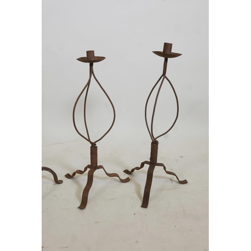 106 - A pair of wrought iron candlesticks on tripod feet, and a pair of similar fire dogs, 22