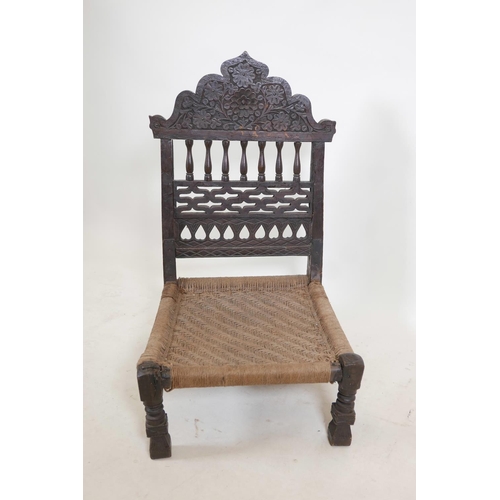 1139 - An antique Indian Pidha chair with a carved and pierced hardwood back, a woven seat, and metal strap... 