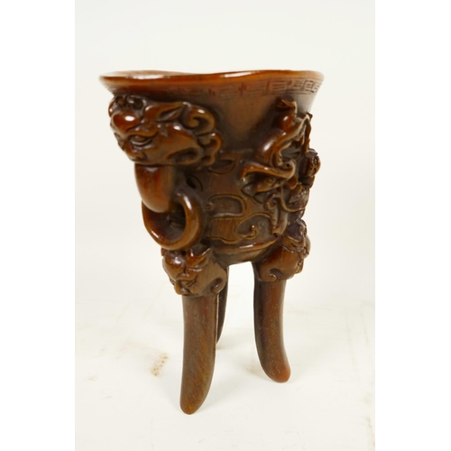 416 - A Chinese faux horn libation cup on three legs, embossed with mythical beasts