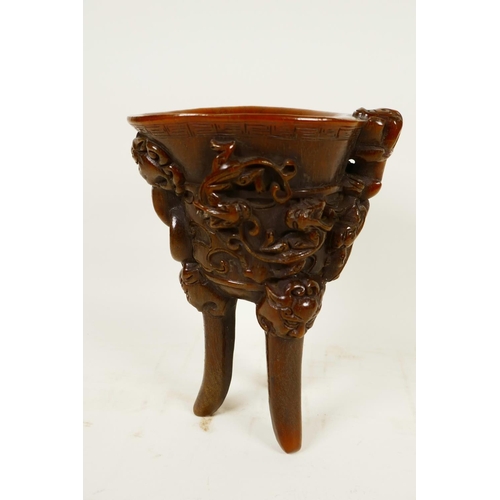 416 - A Chinese faux horn libation cup on three legs, embossed with mythical beasts