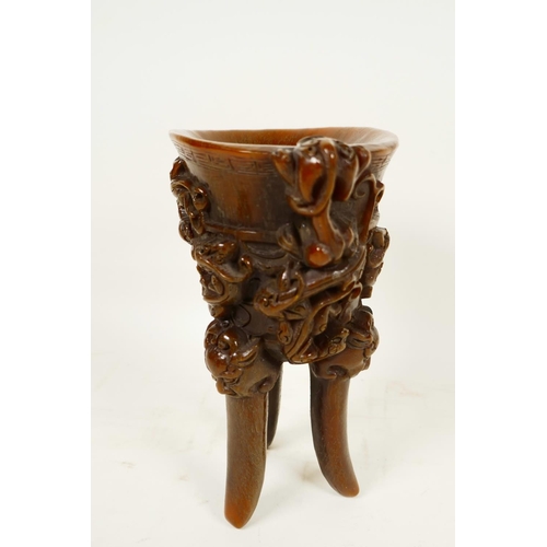 416 - A Chinese faux horn libation cup on three legs, embossed with mythical beasts