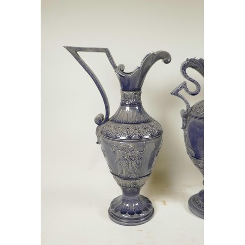 424 - A German pottery garniture consisting of two ewers and matching urn, with an indigo glaze and classi... 