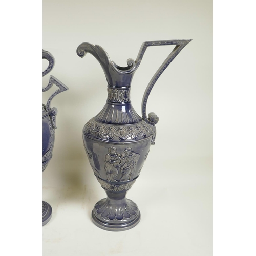 424 - A German pottery garniture consisting of two ewers and matching urn, with an indigo glaze and classi... 