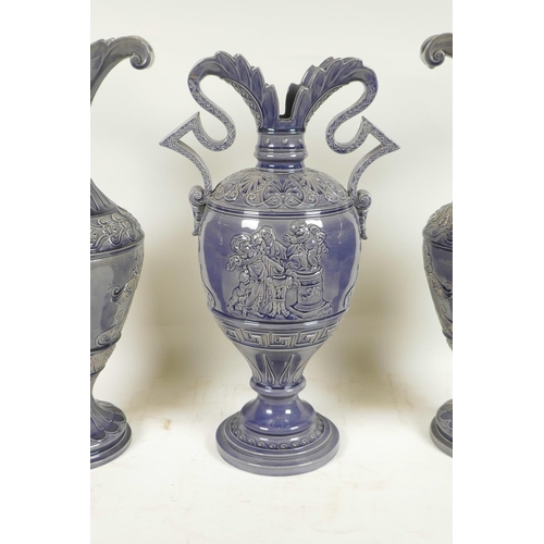 424 - A German pottery garniture consisting of two ewers and matching urn, with an indigo glaze and classi... 