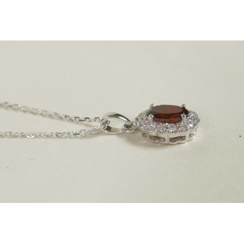 681 - An 18ct white gold pendant necklace set with a garnet encircled by diamonds