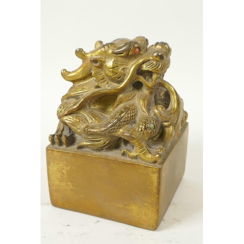 42 - A Chinese gilt bronze seal, the top cast as a mythical creature with coral set eyes, 3½