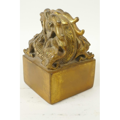 42 - A Chinese gilt bronze seal, the top cast as a mythical creature with coral set eyes, 3½