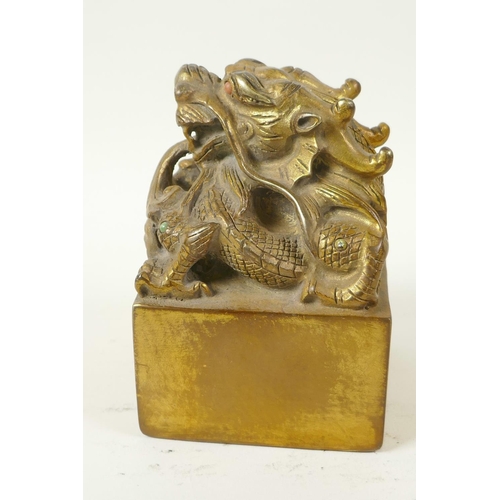 42 - A Chinese gilt bronze seal, the top cast as a mythical creature with coral set eyes, 3½