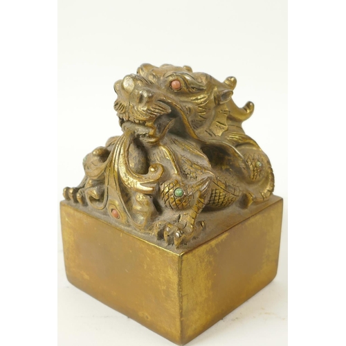 42 - A Chinese gilt bronze seal, the top cast as a mythical creature with coral set eyes, 3½