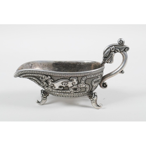 98 - A Chinese white metal libation cup with stylised dragon decoration and tripod feet, mark to base, 5&... 