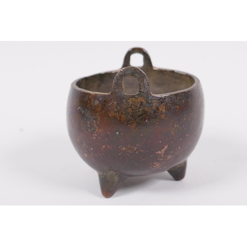 60 - A miniature Chinese bronze cauldron shaped censer with two loop handles and three cast feet, impress... 