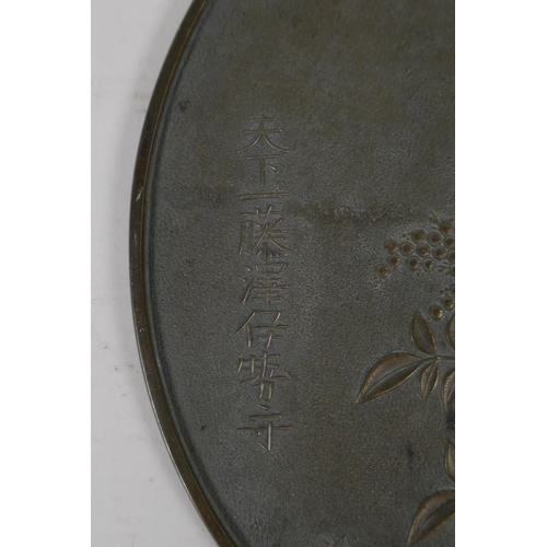 49 - A Japanese bronze hand mirror, decorated with the Mitsudomoe, a fruit bearing bush, and character in... 