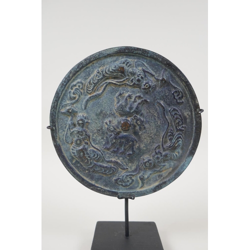 28 - A Chinese bronze archaic style mirror with raised decoration of mythical creatures, on a display mou... 