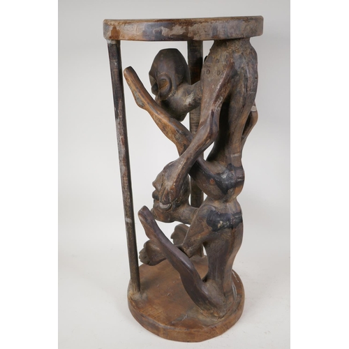 37 - An African hardwood stand, carved as two caged figures, 23½