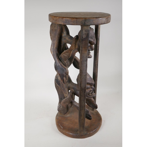 37 - An African hardwood stand, carved as two caged figures, 23½